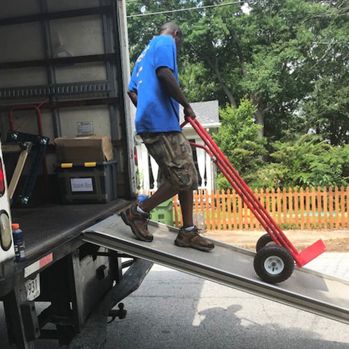 Mover rolling a hand truck of boxes up a moving truck ramp